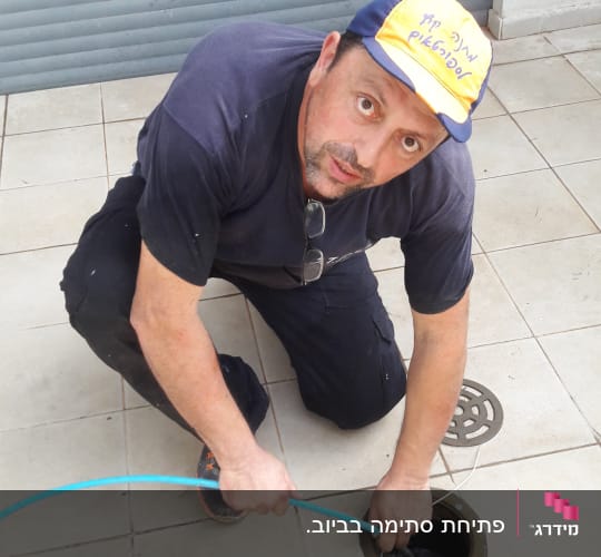 אדם עובד עם צינור ניקוז בפתח ביוב